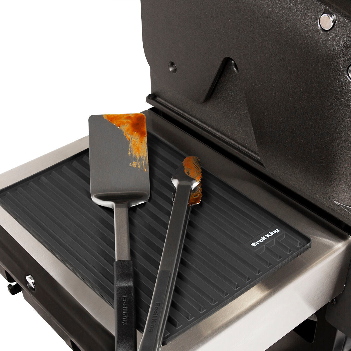 Silicone mat positioned on a grill side shelf beneath separate utensils
