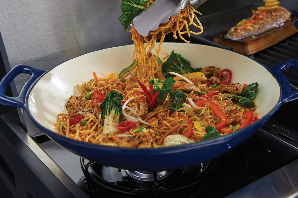 Food cooking in a cast grilling wok on a side burner