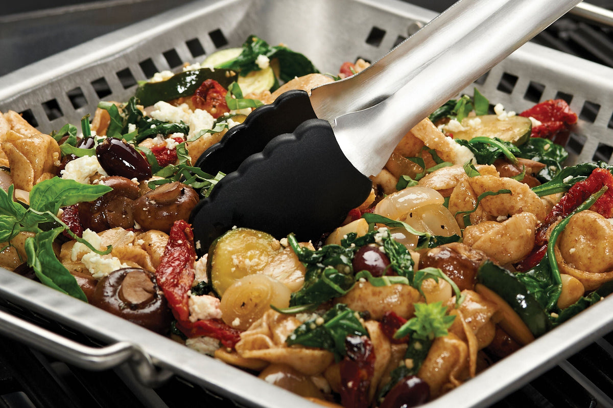 Grill wok holding vegetables while tongs turn the food