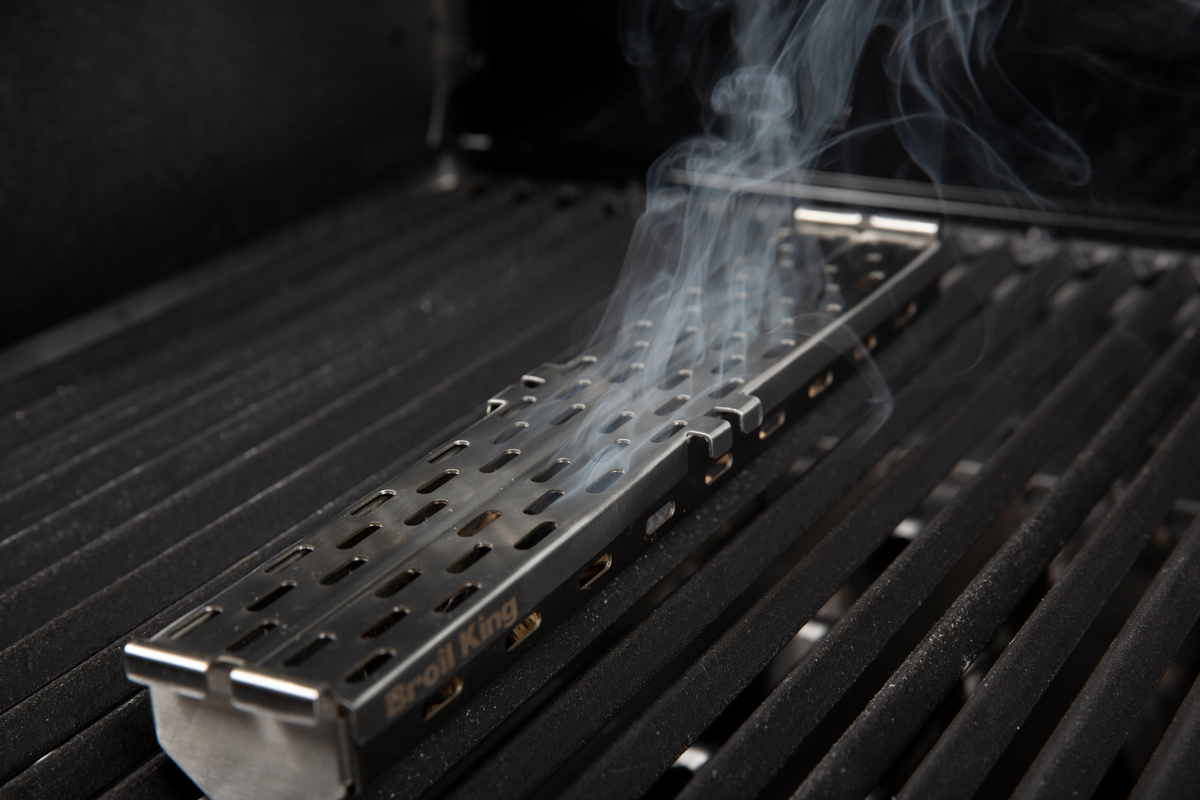 Pellet smoker box producing smoke beneath the cooking grids