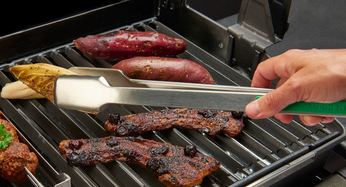 Green-handled grilling tongs turning steak on the grill