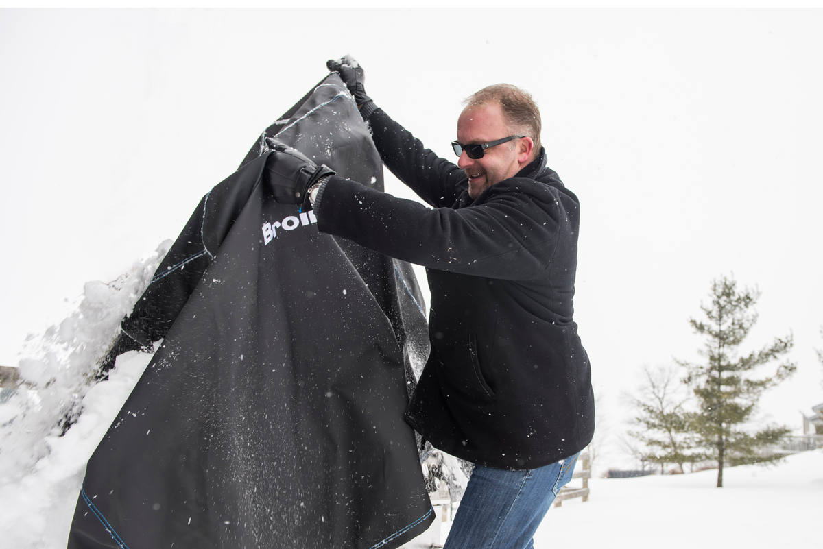 Person lifting a snow-covered grill cover outdoors