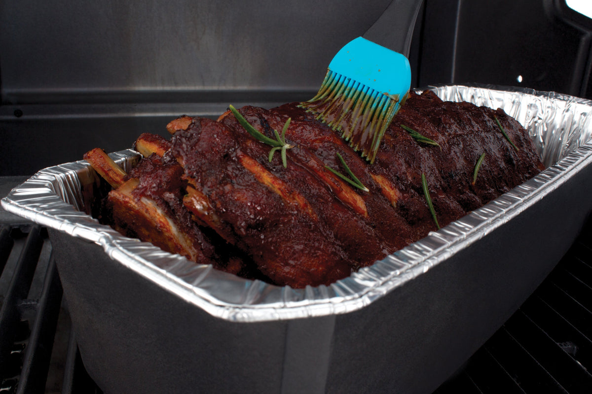 Basting brush applying sauce to ribs in a foil roaster liner