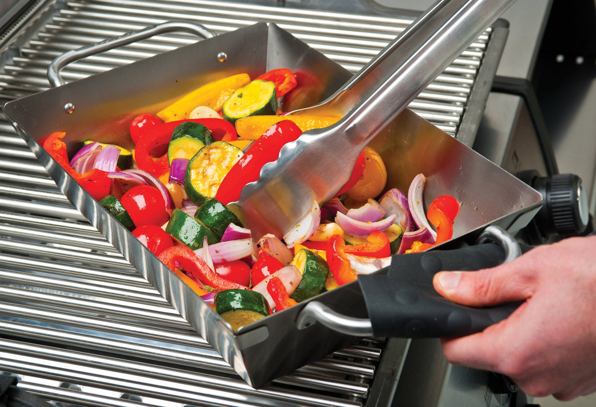 Vegetables being stirred in a deep stainless steel wok on a separate grill