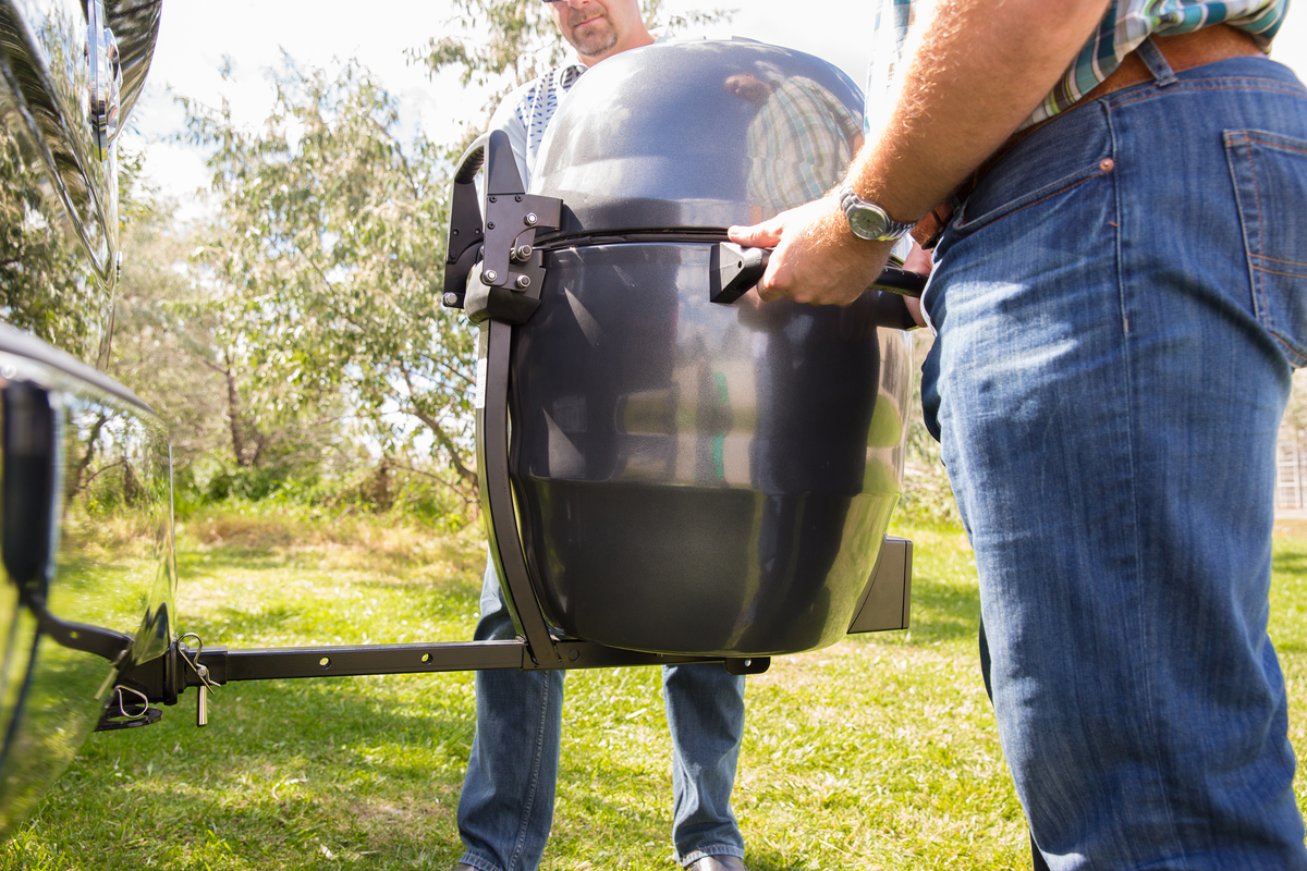 Keg grill carried by its handles beside a vehicle-mounted hitch support