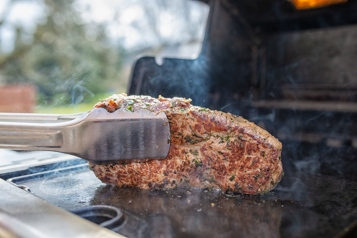 One Imperial grilling tong holding seasoned meat over a separate grill