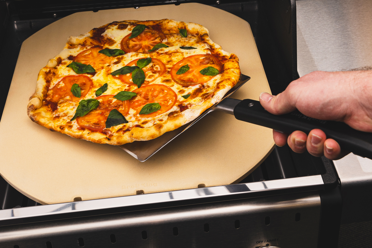 Double-wide flipper lifting a pizza from a separate grilling stone