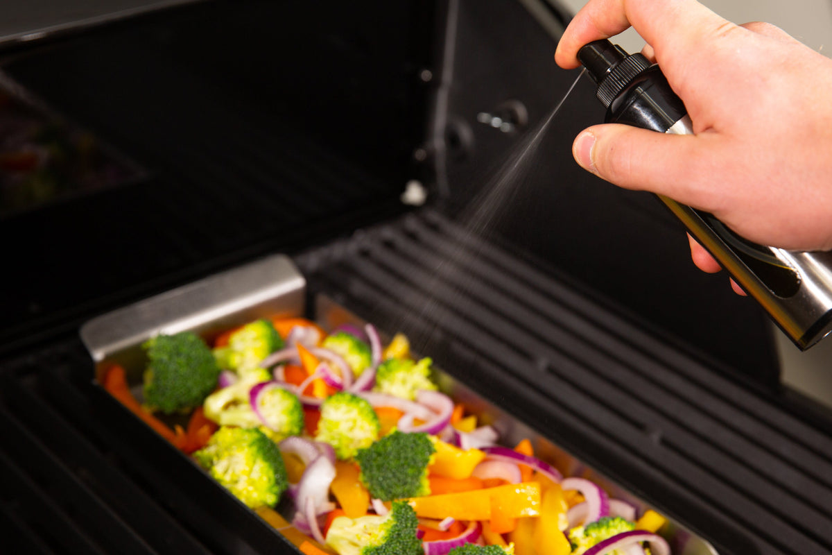 Oil spritzer spraying vegetables in a grill basket