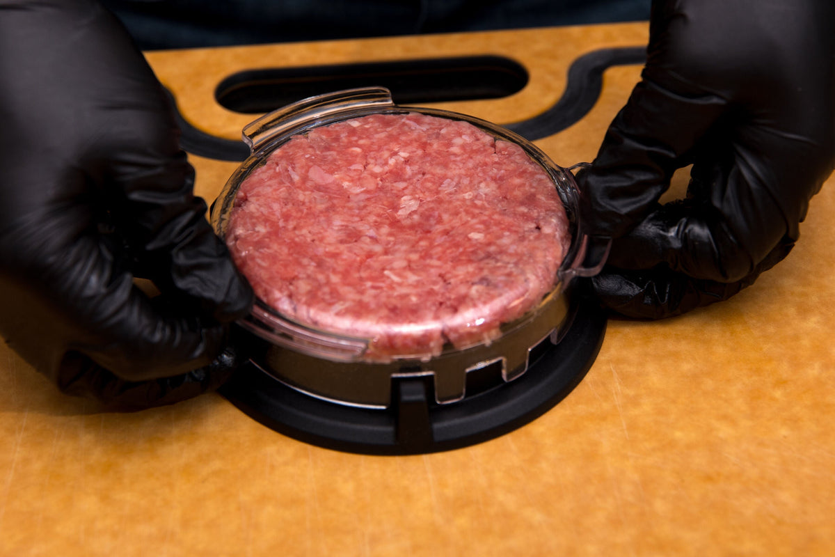 Gloved hands using a press to shape a burger patty