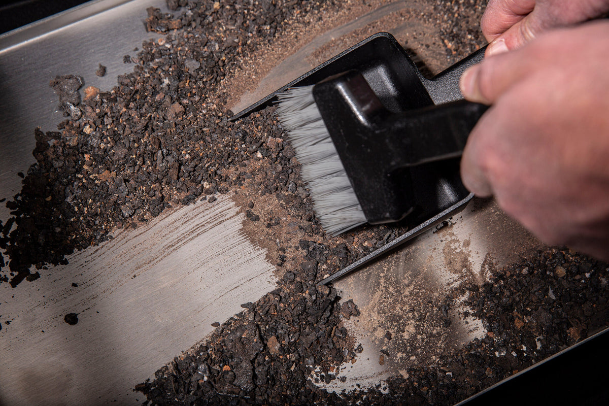 Cleaning brush and dustpan collecting ash inside a pellet grill