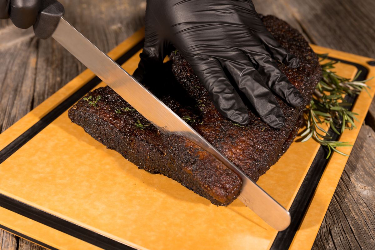 Knife slicing brisket on a wood fiber cutting board