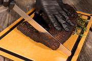 Knife slicing brisket on a wood fiber cutting board