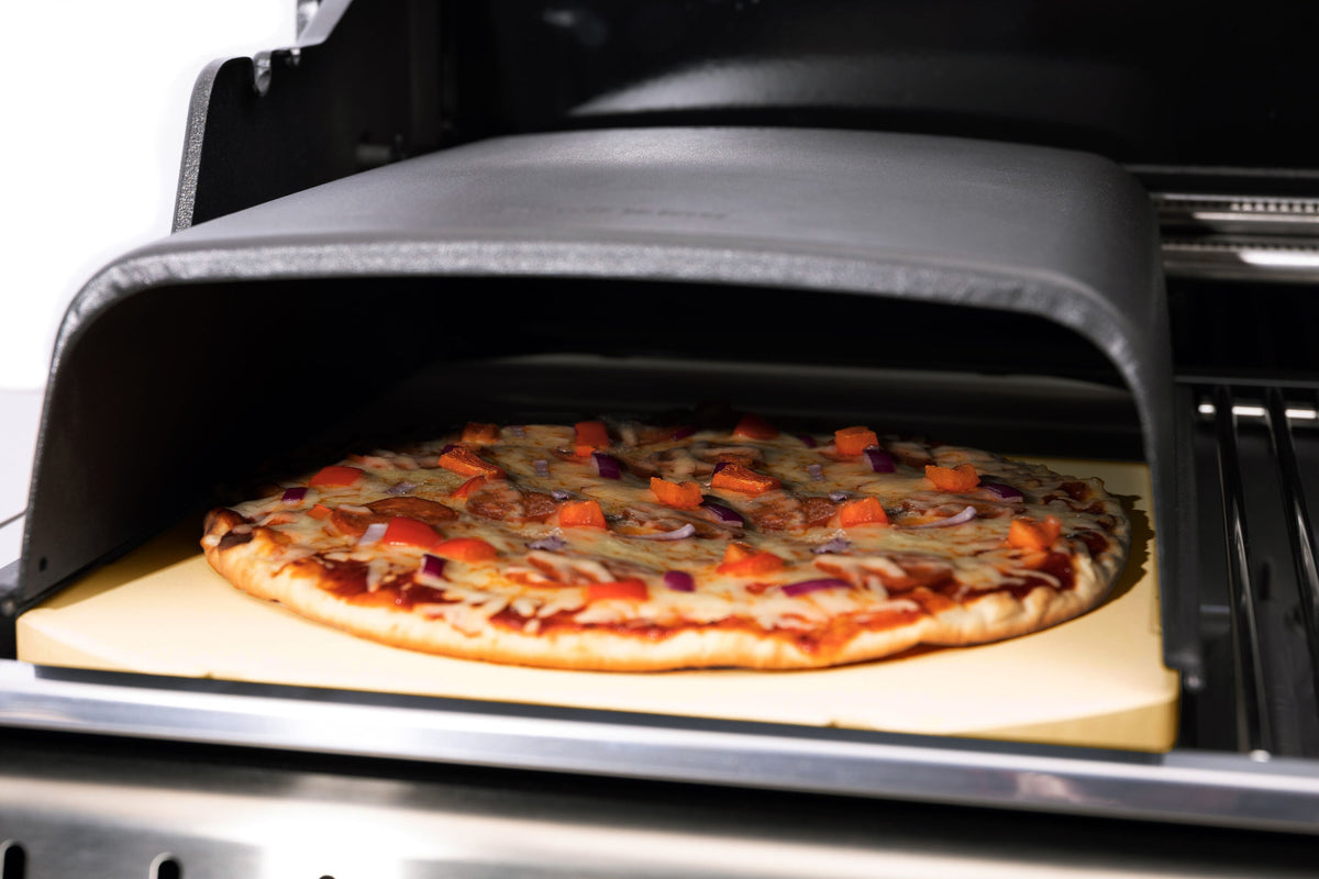 Pizza cooking beneath a cast iron dome on the grill
