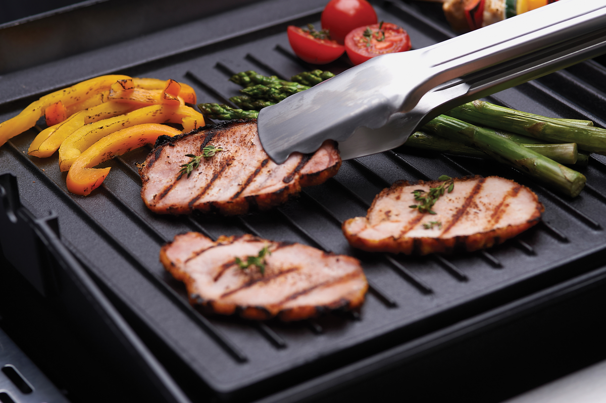 Tongs turning sliced meat on a ribbed griddle