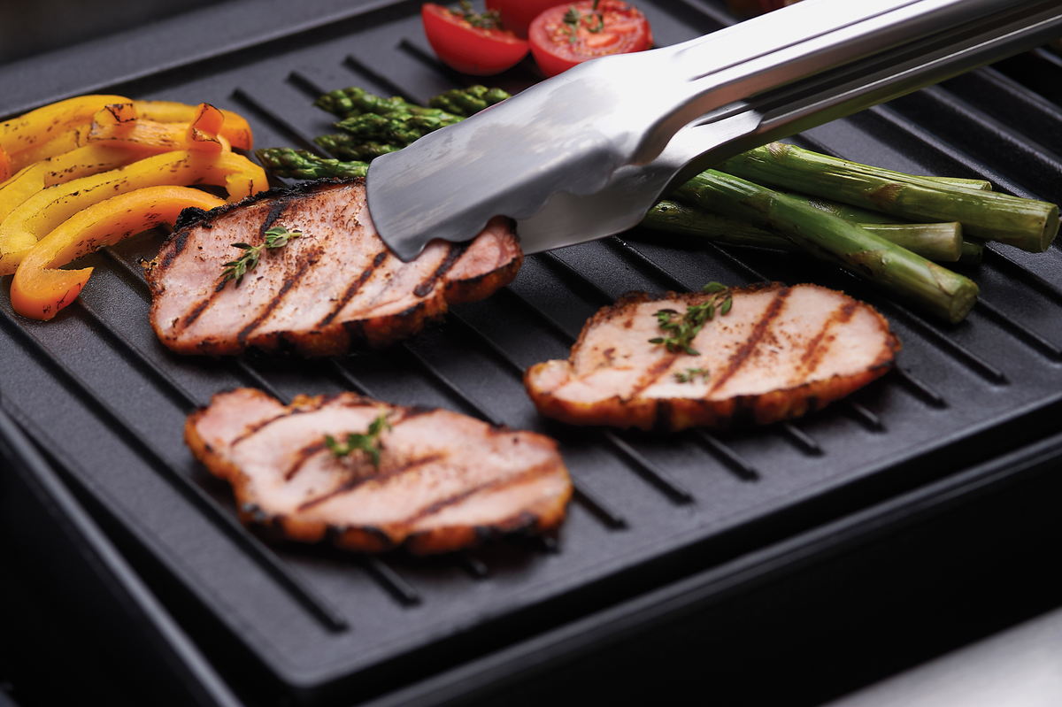 Tongs turning sliced meat on a ribbed griddle