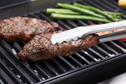 Tongs turning steak on cast iron cooking grids