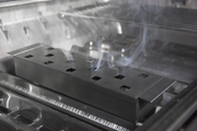 Smoker box producing smoke beneath the cooking grids