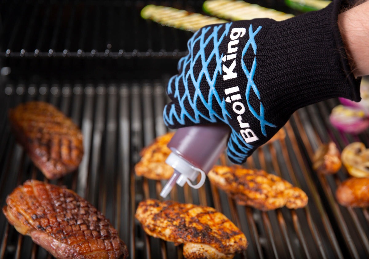 Grilling mitt holding a basting brush over food on the grill