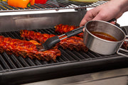 Basting brush applying sauce to ribs beside its sauce bowl