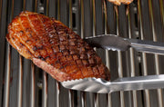 Precision tongs lifting a steak above the cooking grids