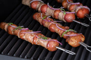Dual-prong skewers holding wrapped sausages on the grill