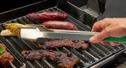 Green-handled grilling tongs turning steak on the grill