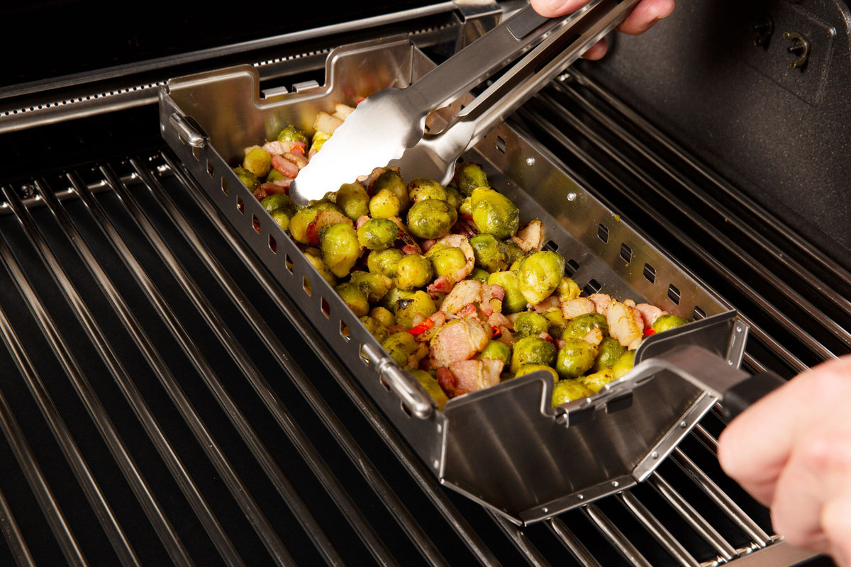 Hand operating a rotisserie tumble basket on the grill