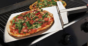Pizza peel holding a cooked pizza beside the grill