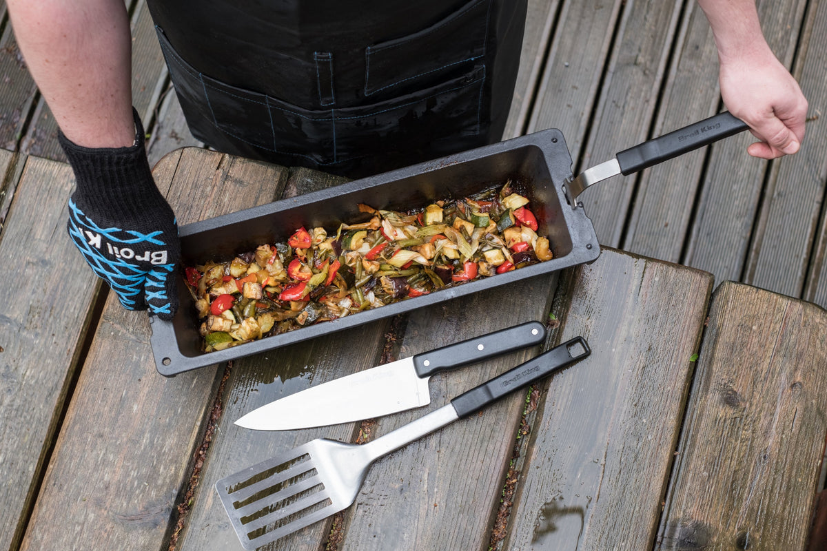 Person holding a cast iron wok filled with vegetables above an outdoor table