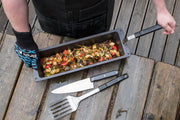 Person holding a cast iron wok filled with vegetables above an outdoor table