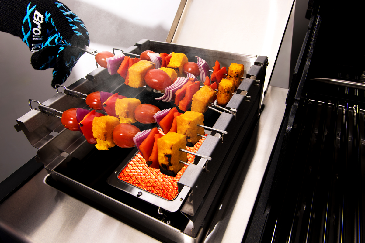 Food skewers cooking above an infrared side burner fitted with a wind shield