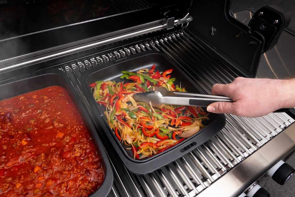 Vegetables being stirred in a cast iron Dutch oven inside a separate grill