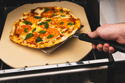 Double-wide flipper lifting a pizza from a separate grilling stone