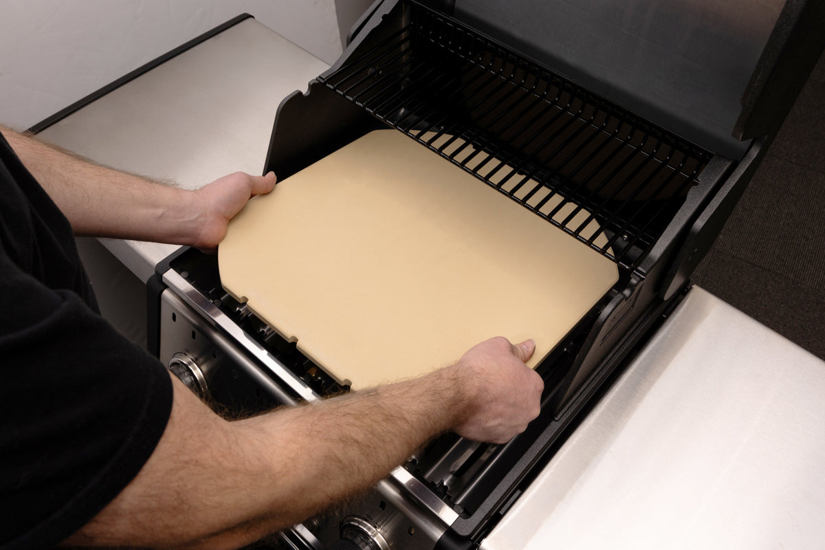 Hands positioning a pizza stone inside a compatible grill