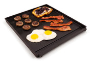 Eggs, bacon, and sausages arranged on a porcelain plancha