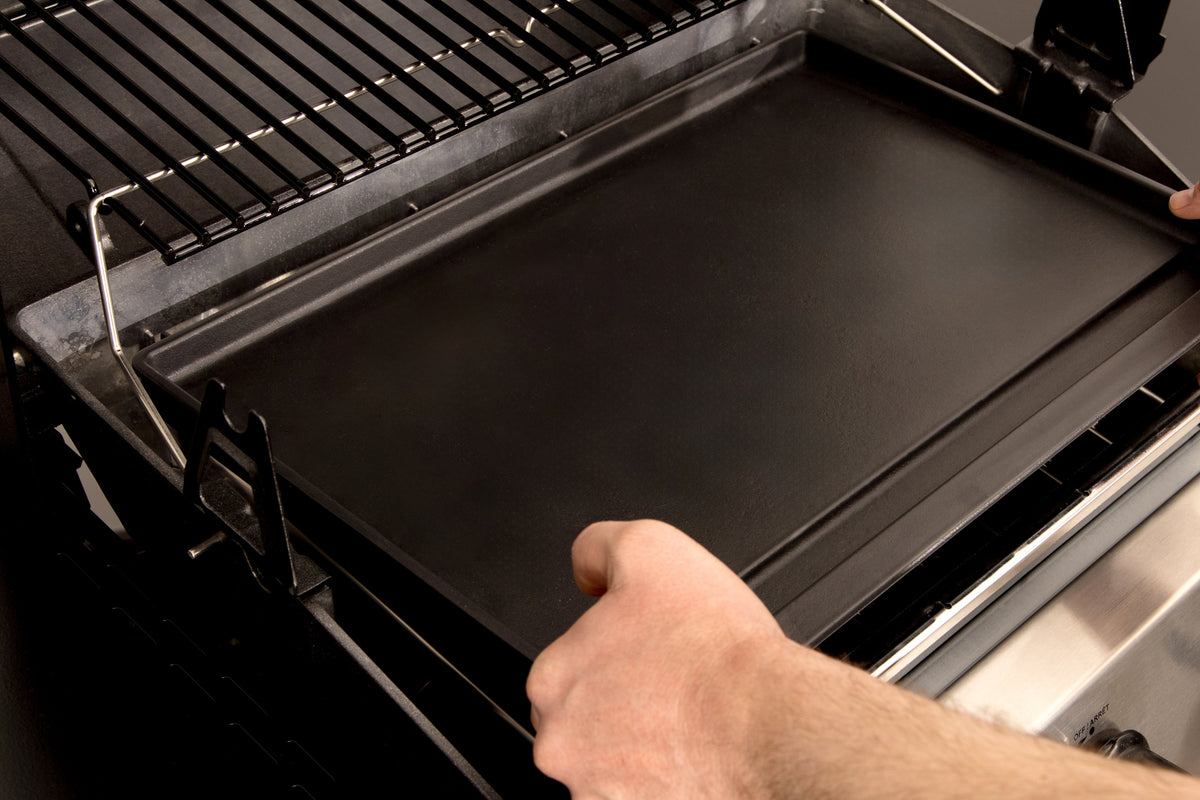 Hand positioning a porcelain plancha inside a grill