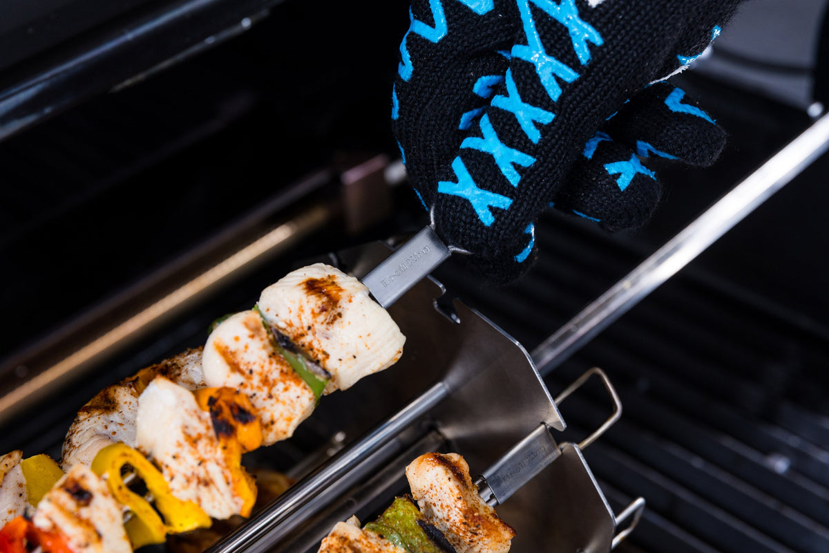 Gloved hand positioning the rotary kebab rack on a grill rotisserie