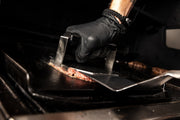 Gloved hand using a smash burger press on a separate cooking surface