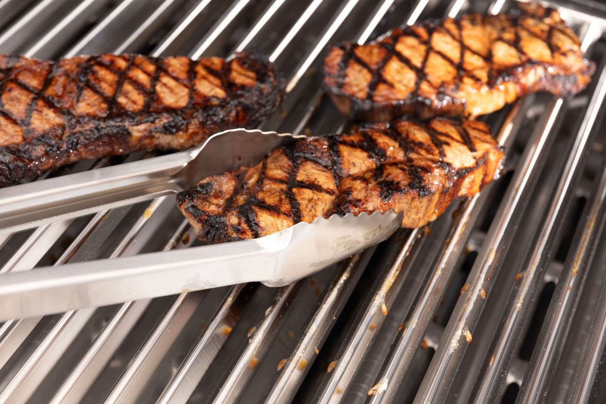 Tongs turning steaks on Baron and Crown V-shaped stainless steel grids