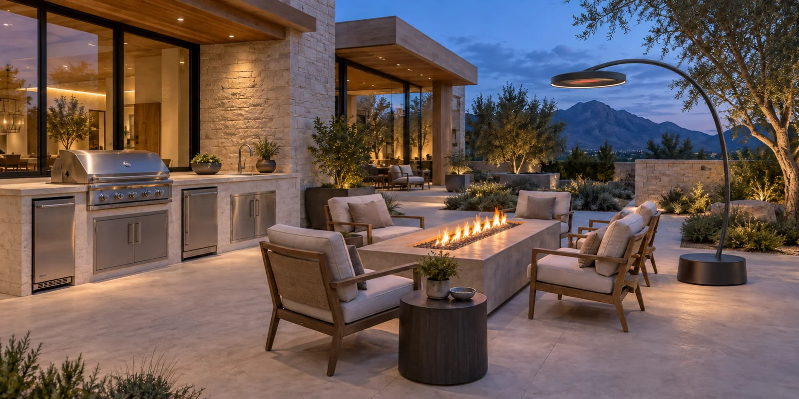 Outdoor kitchen with an uncovered grill, refrigeration, sink and storage beside a lit fire table and a Bromic Eclipse curved-arm freestanding heater